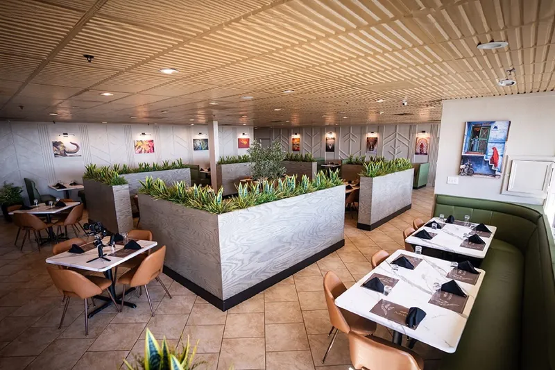 Bright, modern dining room at Aahaa in Overland Park with tan leather chairs, green banquettes, planter dividers and framed photos along the walls