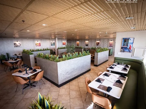 Bright, modern dining room at Aahaa in Overland Park with tan leather chairs, green banquettes, planter dividers and framed photos along the walls
