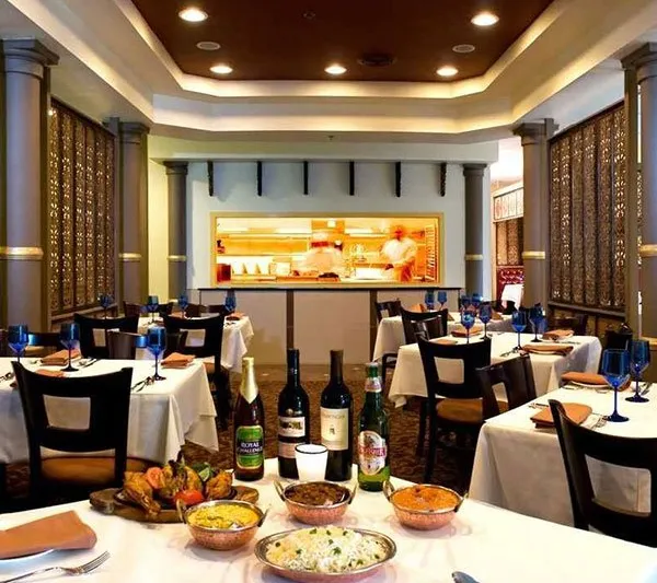 Dining room at The Indian Harvest with set tables, an open kitchen, and Indian dishes in the foreground