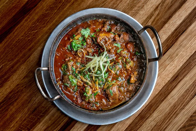 Curry served in a steel karahi on a wooden table at Dhamaka
