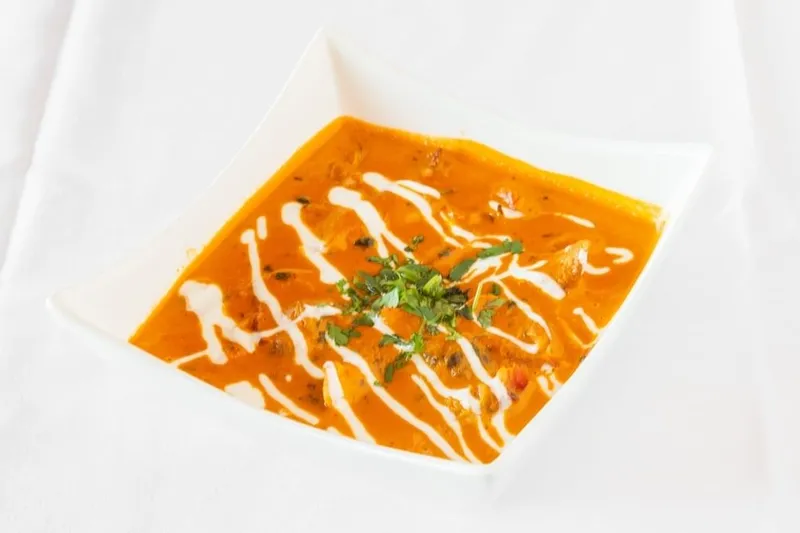 Butter chicken in a creamy tomato sauce swirled with cream and topped with cilantro, served in a white square bowl at Pind Indian Cuisine in Grand Rapids