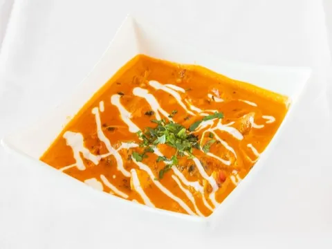 Butter chicken in a creamy tomato sauce swirled with cream and topped with cilantro, served in a white square bowl at Pind Indian Cuisine in Grand Rapids