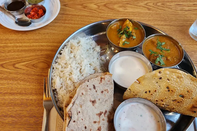 Thali at Shalimar of India in Burlington — a steel platter of basmati rice, two curries, raita, chapati and papad, with a side plate of chutneys, on a wood table