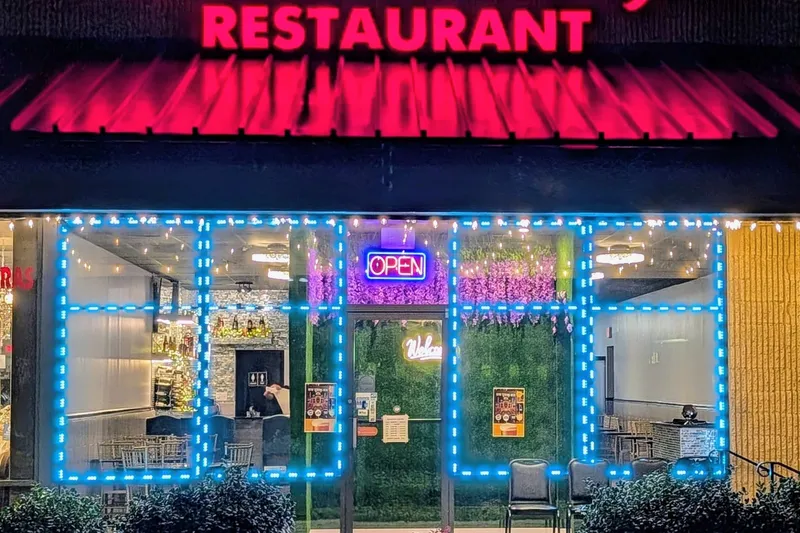 Nighttime storefront of India K'Raja Restaurant at 9051 West Broad Street in Richmond, with a lit red sign, blue string lights framing the windows, and a neon OPEN sign in the door