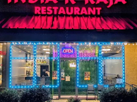 Nighttime storefront of India K'Raja Restaurant at 9051 West Broad Street in Richmond, with a lit red sign, blue string lights framing the windows, and a neon OPEN sign in the door