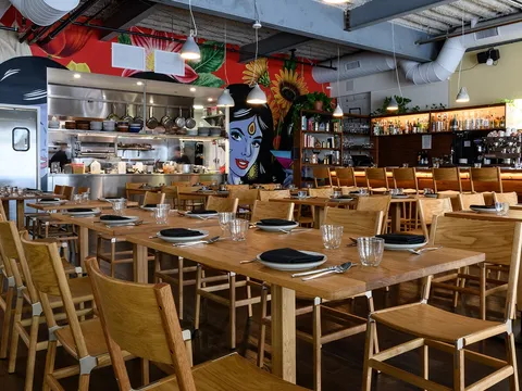 Besharam dining room with wooden tables, open kitchen and colorful wall art