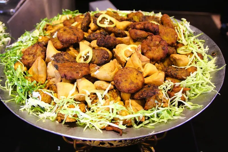A large steel platter of assorted fried Indian appetizers — samosas, pakoras and fritters garnished with shredded cabbage and green chilies — at Taj Mahal Indian Cuisine in Pittsburgh