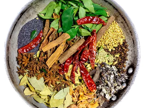 Overhead photo of a metal bowl of whole South Indian spices — curry leaves, dried red chiles, cinnamon, star anise, cardamom, coriander and bay leaves — from Paper Dosa in Santa Fe