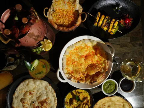 An overhead spread of Indian dishes at Roti Cuisine of India including biryani, tandoori chicken, paneer skewers, curries and naan