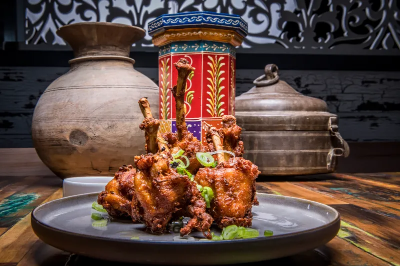 Plate of spiced chicken lollipops garnished with scallions at Bombay Street Kitchen