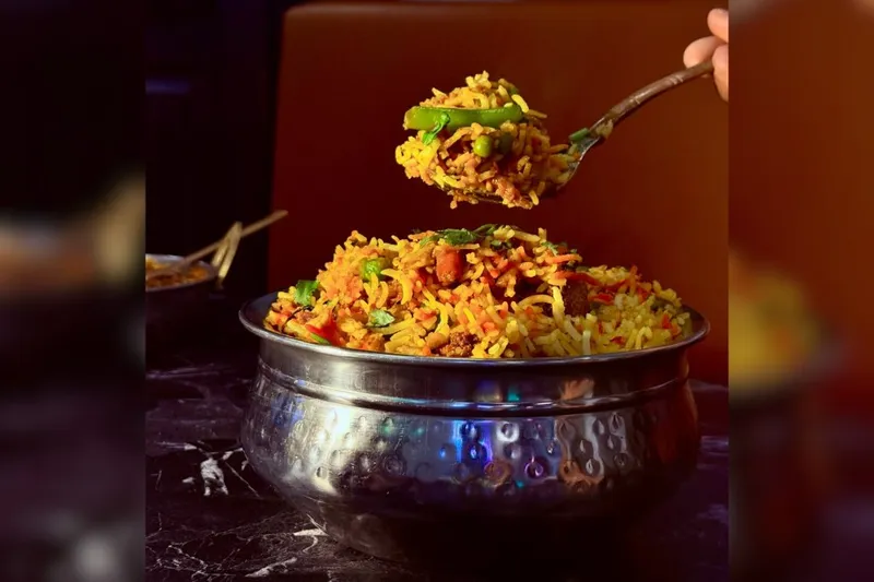 Biryani served in a hammered steel bowl with a spoonful lifted above it, at Panj Tara in Allen